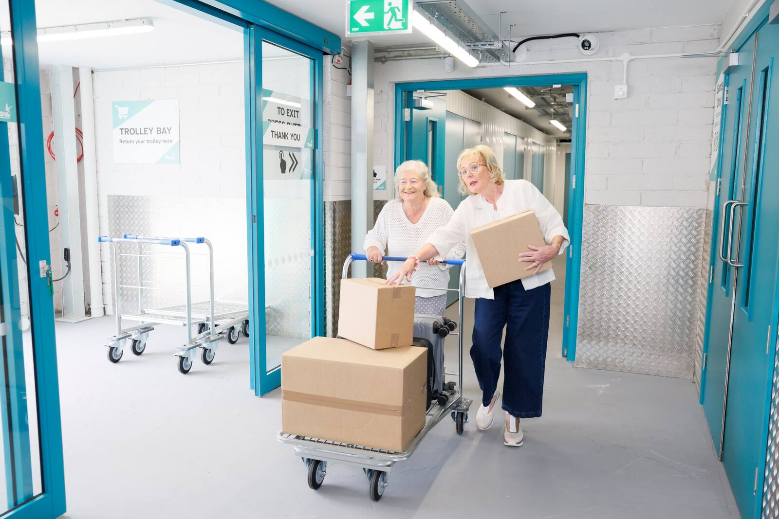 Two customers moving boxes and a suitcase on a trolley at the Stow trolley bay